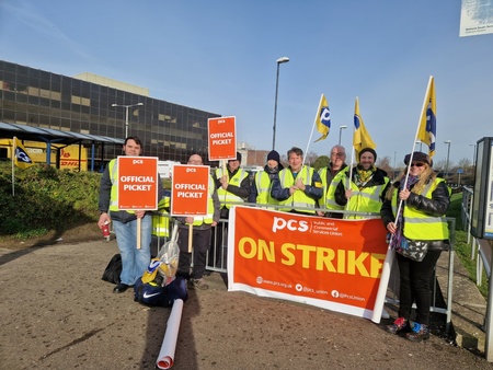 Image shows 8 members with PCS ON STRIKE banner, flags and placards