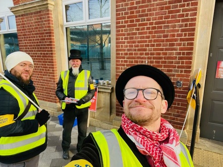 Image shows 3 PCS pickets in high vis vests, two wearing top hats