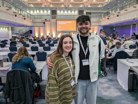The photo shows in the foreground on the left Nat Sherriff, PCS South West Regional Young Members' Convenor, alongside Huz Patel, national young members' committee chair. In the background are delegates to the TUC Young Workers' Conference and a screen with the words: motion 20: tax justice for young workers.