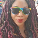 Yemisi has red colours in her long hair and multi-coloured Pride sunglasses