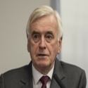 John has short, white hair and is wearing a grey suit and dark red tie