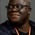 Hector has dark skin, very short, greying hair, and wears glasses