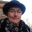 Aitch is wearing a smart black hat with a brim, glasses and a black and white scarf