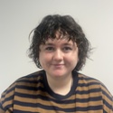 The photo shows Meg who is smiling and has short dark hair and is wearing a striped top