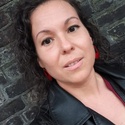 Mariann has dark curly hair and is wearing a black biker style jacket.
