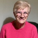 Carole has short, fair hair and glasses. She is smiling at the camera.