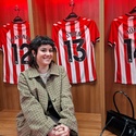 The photo shows young member Molly sat on a bench in the Sunderland dressing room with the red and white striped football shirts hanging behind her