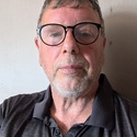 Andrew has grey hair, a short beard and glasses